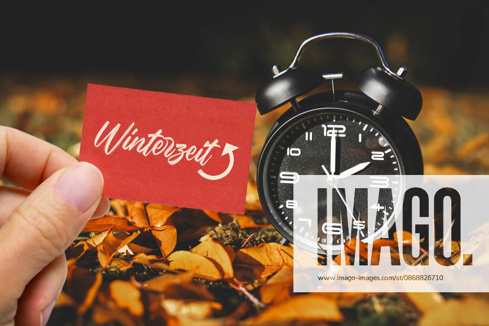 PHOTOMONTAGE: A hand holding a note that reads Winter Time in front of an alarm clock amid autumn leaves; symbolic photo of the time change in Hamburg, Germany ** ** **