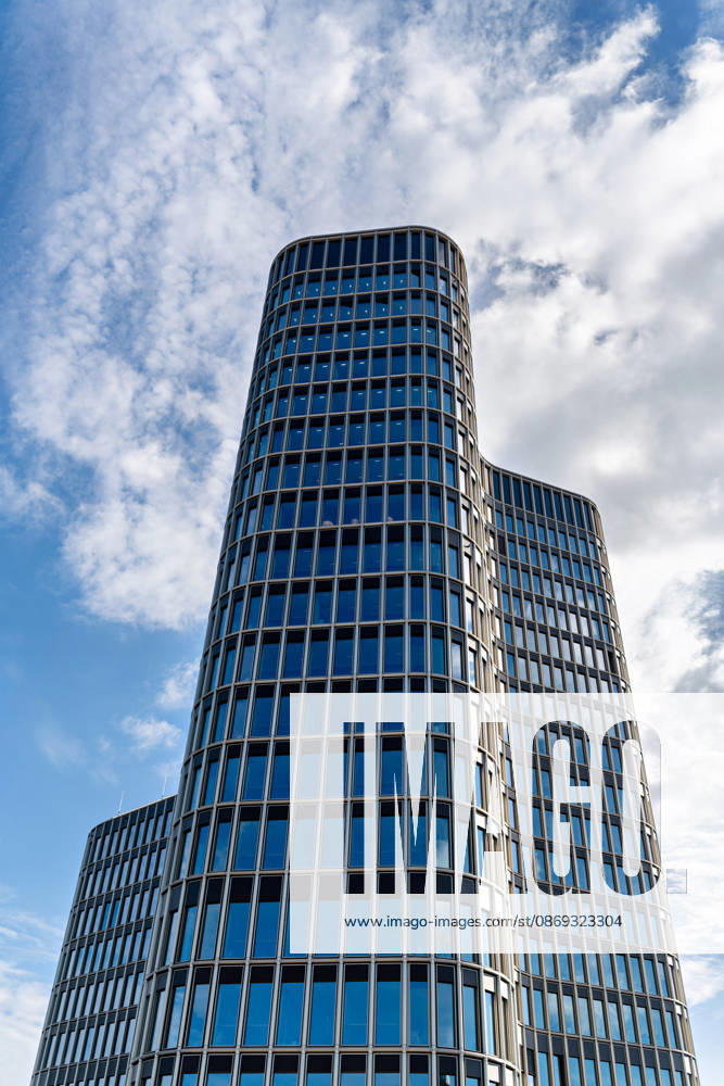 Berlin, 13.10.2026: Blick von unten auf den 19-geschossigen Turm des neuen DKB-Campus an der Heidestraße 26 28 in der Europacity in Berlin-Mitte; die geschwungene Glasfassade hebt sich vor blauem Himmel und Wolken ab. Die Deutsche Kreditbank AG (DKB) hat ihren neuen Hauptsitz heute offiziell eröffnet. Der von Kleihues + Kleihues entworfene, rund 82 Meter hohe Komplex besteht aus drei Gebäudeteilen mit fünf, elf und 19 Geschossen und rund 35.000 Quadratmetern Mietfläche; entwickelt wurde er von der CA Immo unter dem Projektnamen Upbeat. Rund 2.600 Mitarbeitende des DKB-Konzerns, die bislang auf mehrere Berliner Standorte verteilt waren, arbeiten nun gemeinsam im Campus. Die DKB ist Exklusivmieterin und hat einen Mietvertrag übe