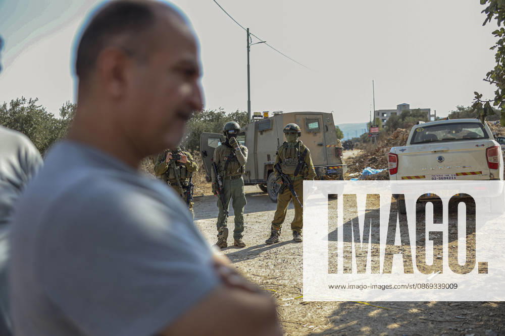 Settlers Disrupt Turmus Ayya Harvest A man stands in the foreground of a dirt road as armed Israeli soldiers stand near an armored vehicle and a white pickup truck in Turmus Ayya, near Ramallah, in the Israeli-occupied West Bank, on October 13, 2026. Palestinian news agency WAFA, citing local sources, reported that Israeli settlers attacked the town and tried to prevent residents from reaching their land to harvest olives. Ramallah West Bank Palestinian Territories