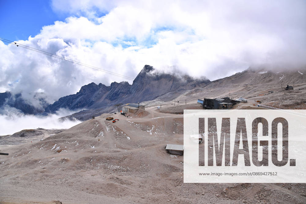 View across the rocky Zugspitzplatt with station buildings, mountain huts, and approaching banks of clouds. Ski resort: The shrinking Schneeferner Glacier on the Zugspitzplatt beneath a thick blanket of clouds