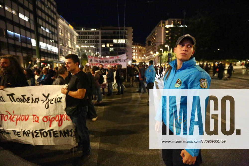 A police officer stands beside demonstrators holding banners during an evening march calling for higher wages and pensions. Athens GREECE - ZUMAx103 20261015_zip_x103_018