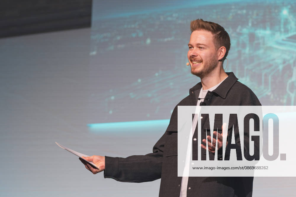 Host Sascha Müller, in high spirits and holding cue cards and a headset microphone, welcomes the audience o