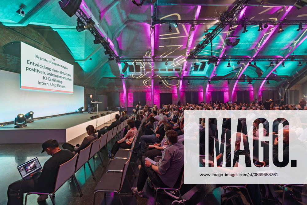 Berlin, 16.10.2026: Teilnehmerinnen und Teilnehmer der NeulandPro Connect 2026 verfolgen in der Halle des WECC den Vortrag von Sascha Lobo, Publizist und Digital-Vordenker; auf der Leinwand die Folie Entwicklung einer einfachen, positiven, unternehmerischen KI-Erzählung. Intern. Und Extern. Die zweitägige KI-Konferenz NeulandPro Connect 2026 findet am 16. und 17. Oktober im Westhafen Event & Convention Center (WECC) in Moabit statt, einem historischen Speichergebäude am Berliner Westhafen. Veranstalter ist NeulandPro, eine Bildungs- und Medienmarke rund um Künstliche Intelligenz. Mit Vorträgen, Workshops und Hackathons richtet sich die Konferenz vor allem an kleine und mittelständische Unternehmen, Gründer und Führungskräfte, die