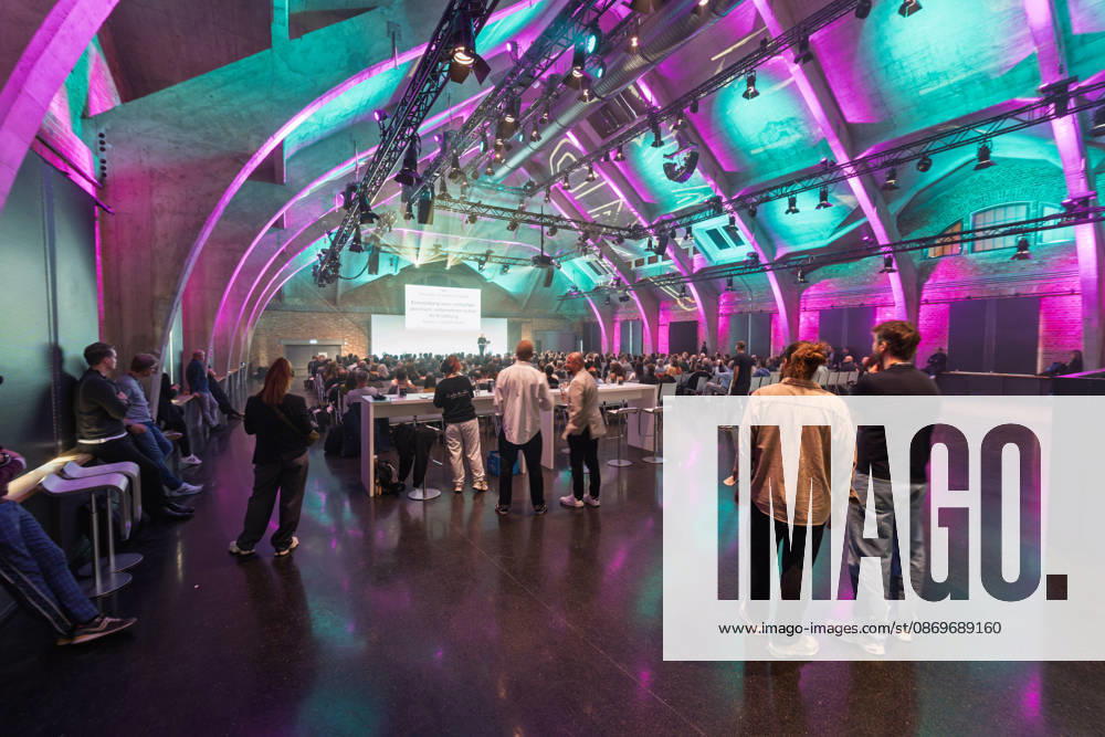 Berlin, 16.10.2026: Teilnehmerinnen und Teilnehmer der NeulandPro Connect 2026 verfolgen in der vollen Halle des WECC stehend und sitzend den Vortrag des Publizisten und Digital-Vordenkers Sascha Lobo. Die zweitägige KI-Konferenz NeulandPro Connect 2026 findet am 16. und 17. Oktober im Westhafen Event & Convention Center (WECC) in Moabit statt, einem historischen Speichergebäude am Berliner Westhafen. Veranstalter ist NeulandPro, eine Bildungs- und Medienmarke rund um Künstliche Intelligenz. Mit Vorträgen, Workshops und Hackathons richtet sich die Konferenz vor allem an kleine und mittelständische Unternehmen, Gründer und Führungskräfte, die KI praktisch einsetzen wollen; erwartet werden bis zu 1.000 Gäste. NeulandPro Connect 2026