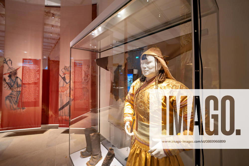 A doll in a display case wears a magnificent yellow silk gown with elaborate embroi