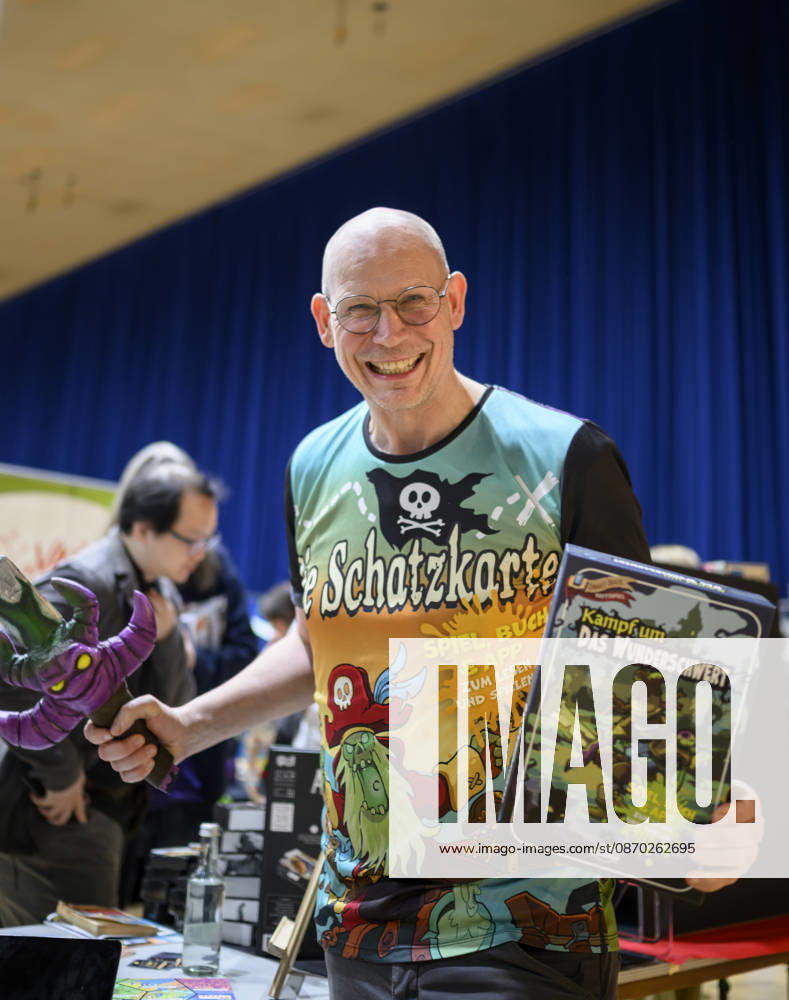 An employee presents the game *Battle for the Magic Sword* by Peasoup Denmark—a 3-in-1 game combining a gamebook, board game, and interactive app— New Product Showcase, on October 21, 2026, at the SPIEL Essen trade show from October 22–25, 2026, in Essen, Germany, at the Grugahalle