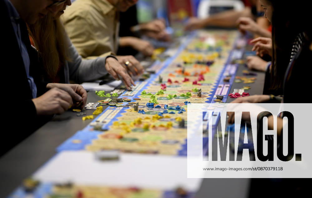 Visitors are playing *The Settlers of Catan* (Kosmos) at a long table, a game table, on October 22, 2026, at the SPIEL Essen trade fair, which runs from October 22 to October 25, 2026, in Essen, Germany, at the Grugahalle.