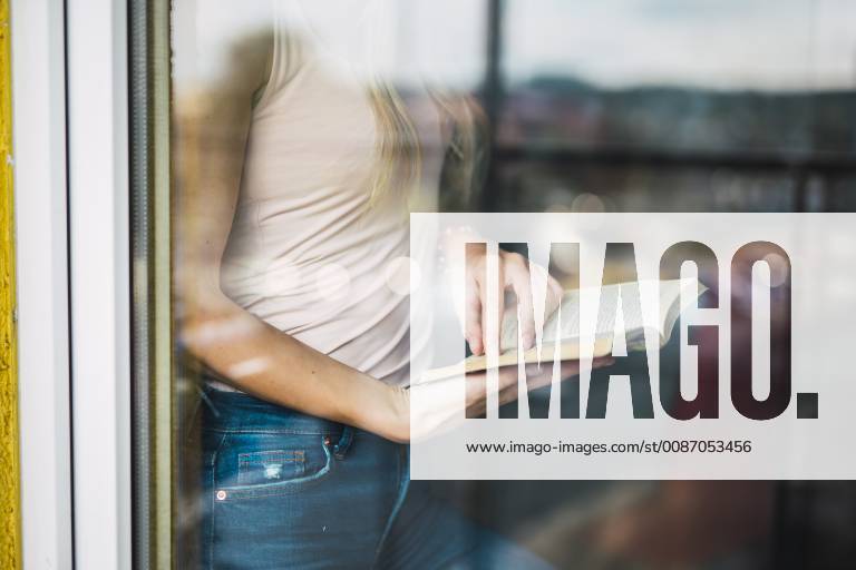 Close-up of young woman reading a book behind windowpane model released Symbolfoto property released KKAF01992