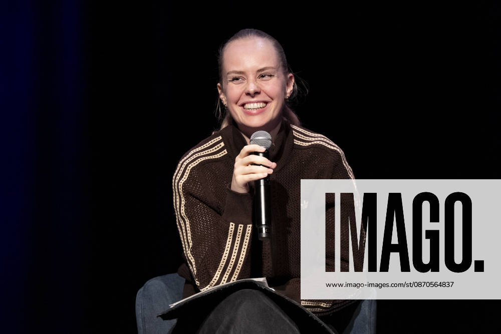 Poetry artist and author Clara LOESEL LÖSEL smiling, laughing, during her reading—a preview event for her new book, *Ich dachte, sowas fühle nur ich*—seated, holding a microphone; single frame, single photo, at the Theater am Tanzbrunnen, Cologne, on October 23, 2026