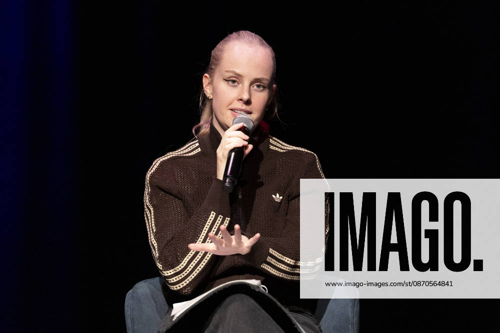 Poetry artist and author Clara LOESEL LÖSEL, looking serious and focused, making a gesture with her hand during her reading—a preview event for her new book, *Ich dachte, sowas fühle nur ich*—seated with a microphone; single frame, single photo, at the Theater am Tanzbrunnen, Cologne, on October 23, 2026
