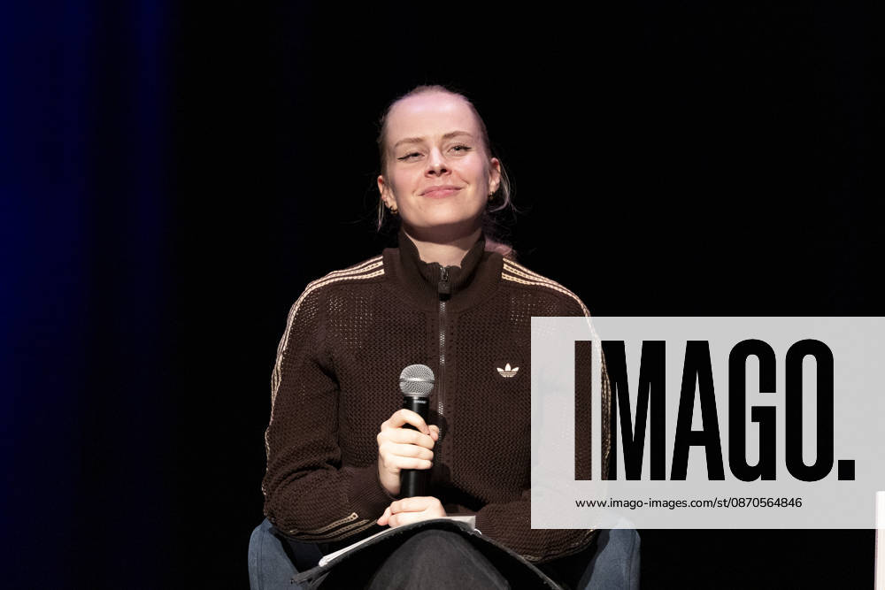 Poetry artist and author Clara LOESEL LÖSEL, smiling, savors the moment during her reading—a preview of her new book, *I Thought I Was the Only One Who Felt This Way*—sitting with a microphone, a single frame, a single photo, at the Theater am Tanzbrunnen, Cologne, on October 23, 2026