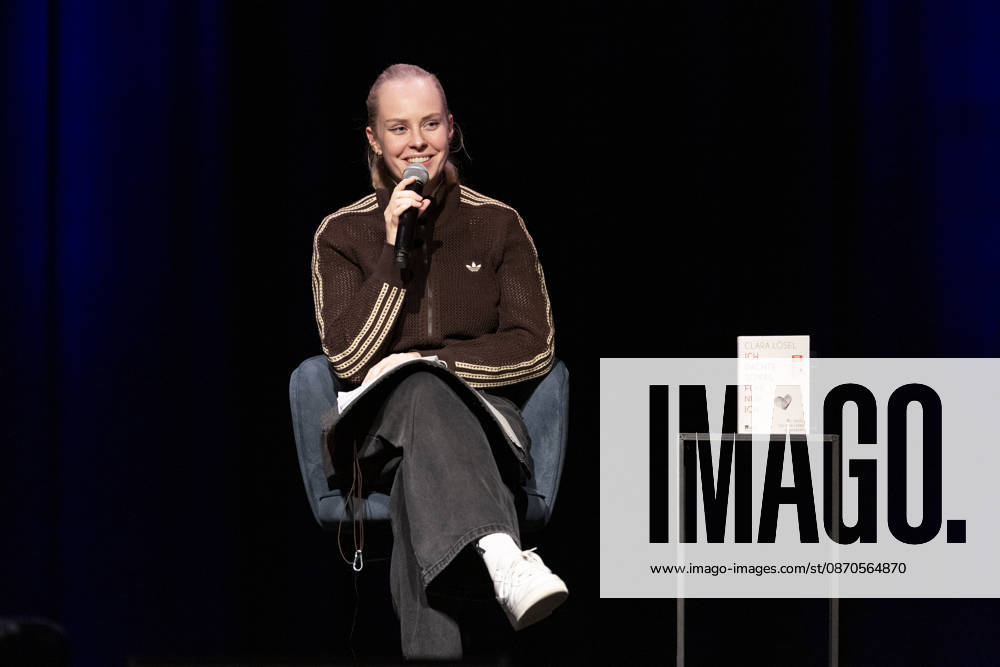 Poetry artist and author Clara LOESEL LÖSEL laughing during her reading, a preview show for her new book *Ich dachte, sowas fühle nur ich* (I Thought I Was the Only One Who Felt That Way), seated with a microphone; single frame, single photo, at the Theater am Tanzbrunnen, Cologne, on October 23, 2026