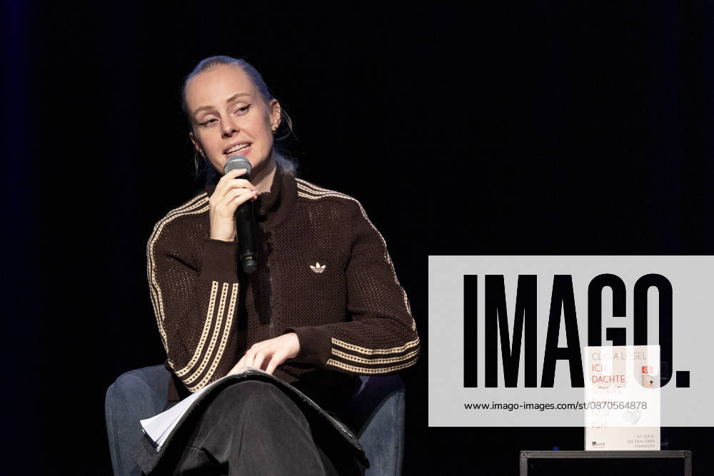 Poetry artist and author Clara LOESEL LÖSEL reading during her reading event, a preview show for her new book, *Ich dachte, sowas fühle nur ich* (I Thought I Was the Only One Who Felt That Way), seated with a microphone; single frame, single photo, at the Theater am Tanzbrunnen in Cologne on October 23, 2026