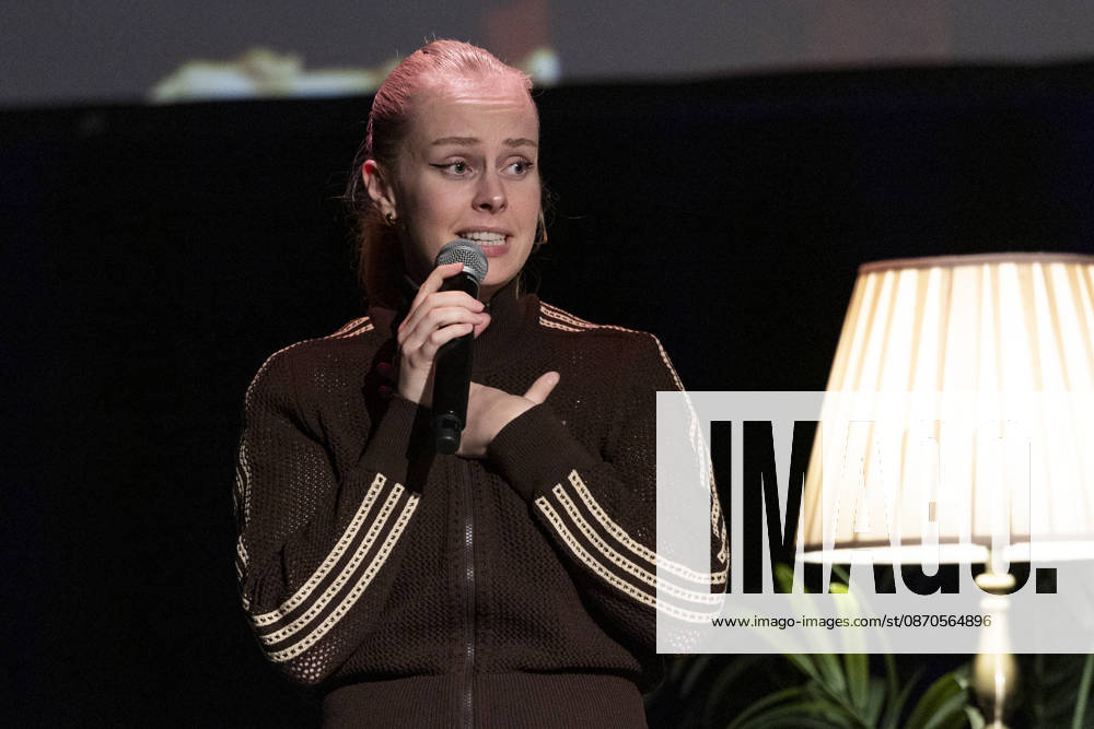 Poetry artist and author Clara LOESEL LÖSEL speaks intently during her reading—a preview of her new book, *Ich dachte, sowas fühle nur ich*—standing with a microphone, in a single frame, a single photograph, at the Theater am Tanzbrunnen, Cologne, on October 23, 2026
