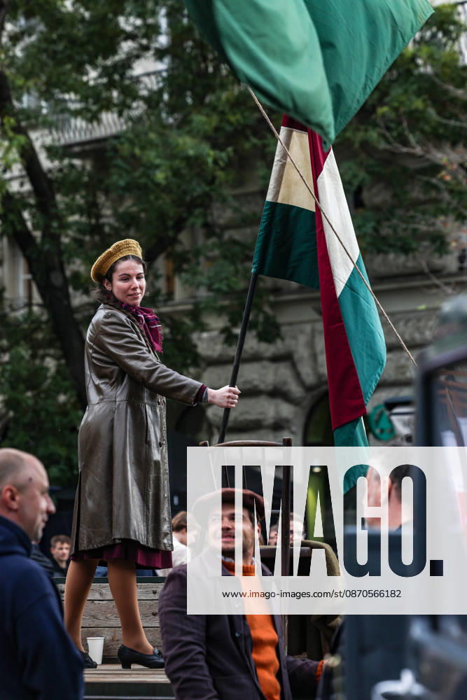 A young woman dressed in period clothing smiles as she holds a Hungarian flag during a historical reenactment commemorating the 70th anniversary of the 1956 Hungarian Revolution. Her beret-style hat and clothing evoke the iconic photographs of young female revolutionaries. Budapest Hungary - ZUMAo116 20261023_znp_o116_008