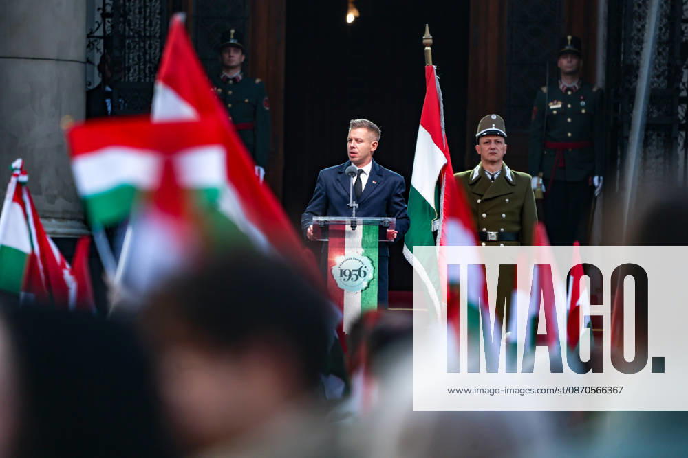 Framed by Hungarian flags, Hungarian Prime Minister PETER MAGYAR speaks during a ceremony marking the 70th anniversary of the 1956 Hungarian Revolution outside Parliament, as ceremonial guards stand beside and behind him. Budapest Hungary - ZUMAo116 20261023_znp_o116_034