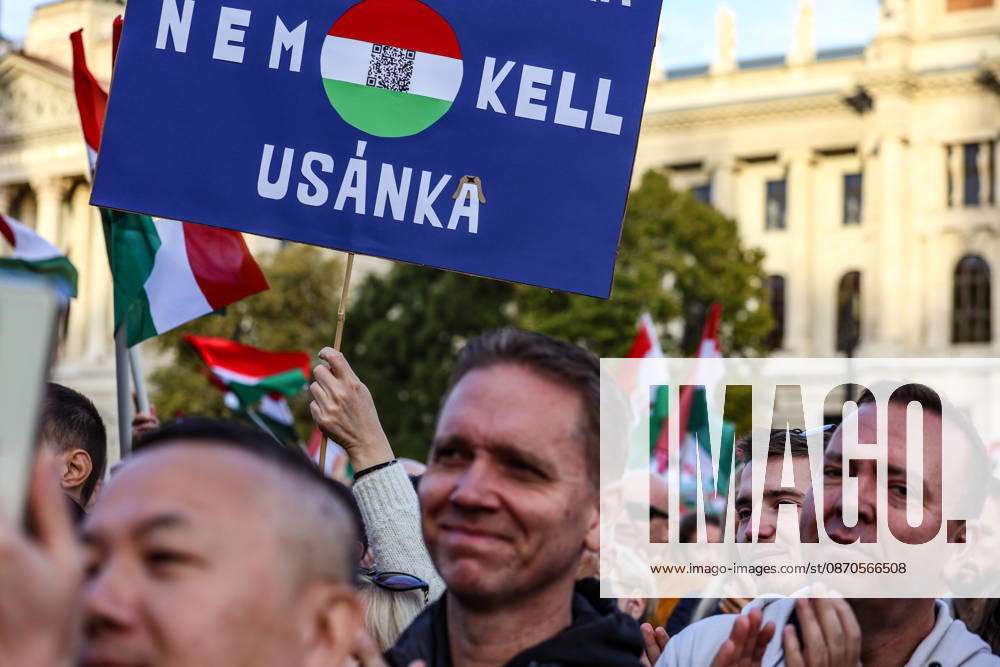 A participant holds a sign reading Nem kell usanka (We dont need a fur hat), referring to the Russian-style military headwear associated with Soviet influence, as crowds wave Hungarian flags during commemorations marking the 70th anniversary of the 1956 Hungarian Revolution outside Parliament. Budapest Hungary - ZUMAo116 20261023_znp_o116_071