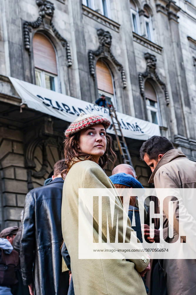 A woman wearing a patterned beret looks over her shoulder during a historical reenactment of the 1956 Hungarian Revolution, with a Hungarian Free Radio banner hanging from a building in the background. The banner recalls the independent radio broadcasts that challenged communist control of information during the uprising against Soviet-backed rule, commemorated on its 70th anniversary. Budapest Hungary - ZUMAo116 20261023_znp_o116_082