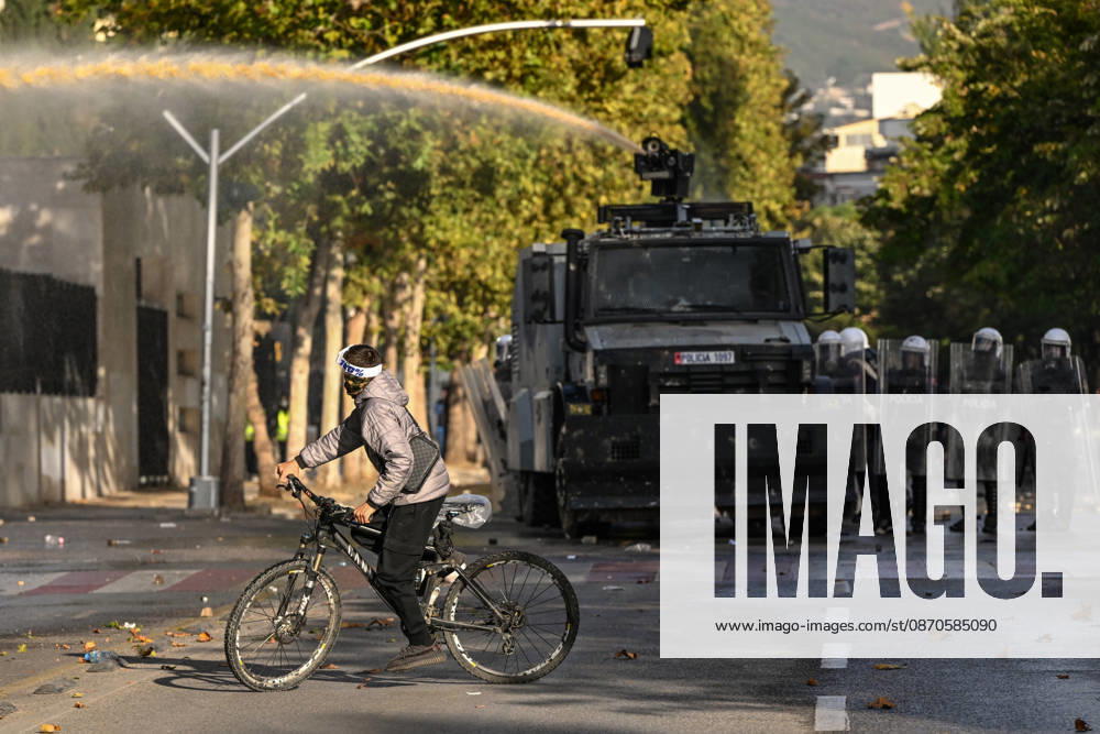Mass Anti-Government National Protest in Tirana TIRANA, ALBANIA - OCTOBER 24: A masked cyclist rides across a debris-strewn intersection as an armored vehicle streams a high-pressure water cannon in the background on October 24, 2026, in Tirana, Albania. Unrest and physical confrontations erupt in Tirana city center as demonstrators and riot police clash during a massive nationwide protest, turning the capital s main avenue into a major flashpoint as chaotic skirmishes broke out between security forces and factions of the crowd. Artur Widak Anadolu Tirana Albania. Editorial use only. Please get in touch for any other usage.