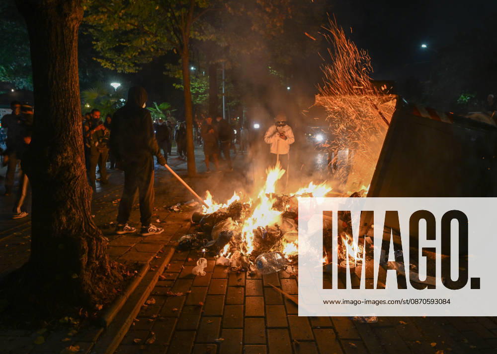 Mass Anti-Government National Protest in Tirana TIRANA, ALBANIA - OCTOBER 24: Masked individuals use a long pole to stoke a large dumpster fire burning on a city sidewalk at night on October 24, 2026, in Tirana, Albania. Unrest and physical confrontations erupt in Tirana city center as demonstrators and riot police clash during a massive nationwide protest, turning the capital s main avenue into a major flashpoint as chaotic skirmishes broke out between security forces and factions of the crowd. Artur Widak Anadolu Tirana Albania. Editorial use only. Please get in touch for any other usage.