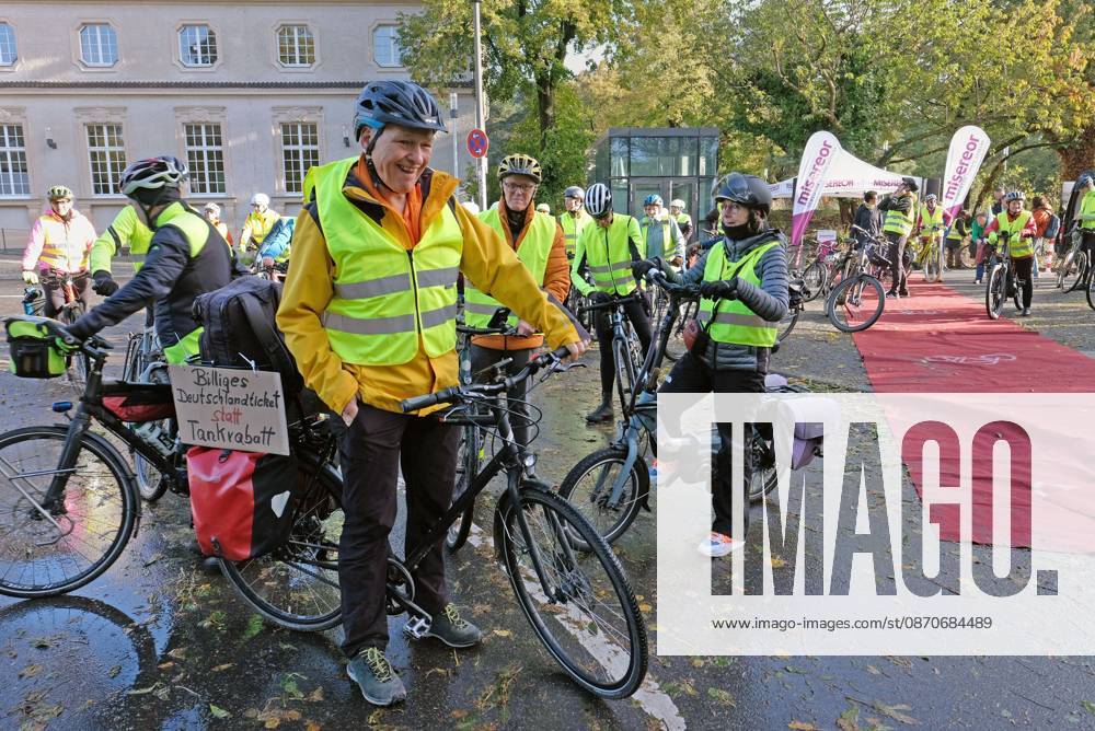 Event coordinator holding a sign reading Affordable Germany Ticket Instead of Gas Rebates in Aachen, October 25, 2026: Start of the Road2COP31 bike ride from Aachen to Antalya—shifting into high gear for climate justice from Aachen to Passau. A