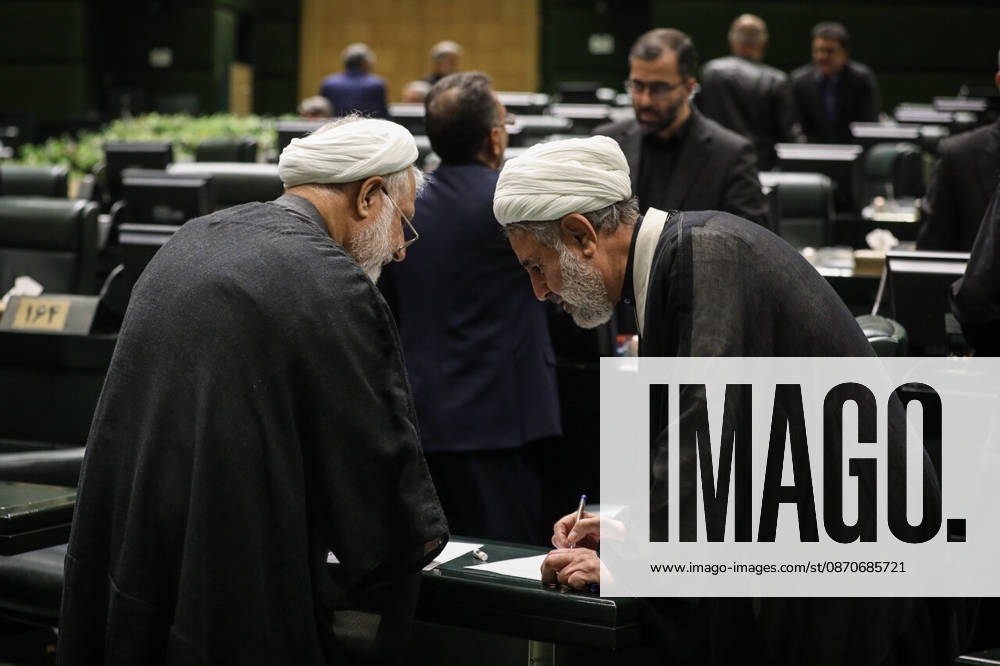 Two white-turbaned clerics lean over a parliamentary desk and examine a document as a man stands behind them at the Islamic Consultative Assembly in Tehran, Iran, on October 25, 2026. The Iranian parliament held a hybrid open sitting, with some lawmakers attending in the Tehran chamber and others participating remotely, according to parliamentary reports. Tehran Iran - ZUMAi98_ 20261025_zih_i98_032