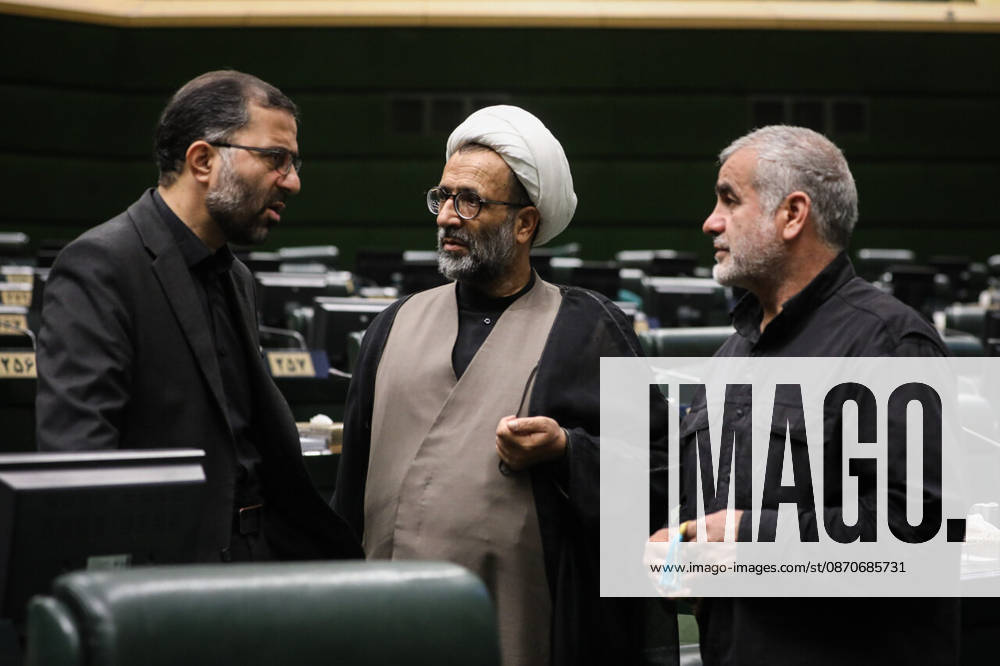 A cleric in a white turban gestures while talking with two men dressed in black beside the green parliamentary seats at the Islamic Consultative Assembly in Tehran, Iran, on October 25, 2026. Parliamentary reports said more than two-thirds of lawmakers joined the October 25 open sitting of the Islamic Consultative Assembly, attending either in person or remotely. Tehran Iran - ZUMAi98_ 20261025_zih_i98_036