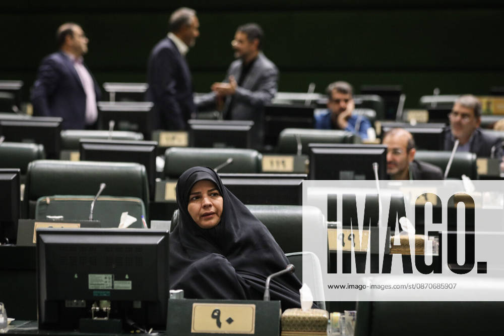 A woman in a black chador sits at her numbered desk while lawmakers converse in the rows behind her at the Islamic Consultative Assembly in Tehran, Iran, on October 25, 2026. Speaker Mohammad Bagher Ghalibaf chaired the October 25 session, which combined physical attendance at the Islamic Consultative Assembly with participation by video link. Tehran Iran - ZUMAi98_ 20261025_zih_i98_053
