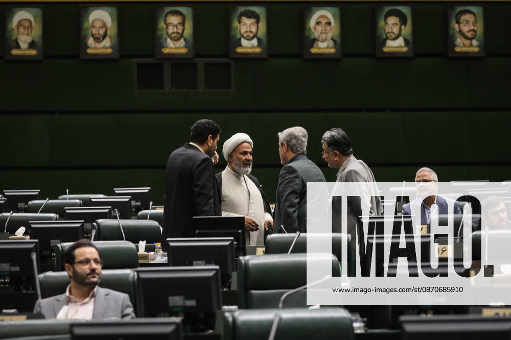 A white-turbaned cleric talks with a group of men in the center of the chamber beneath a row of framed portraits at the Islamic Consultative Assembly in Tehran, Iran, on October 25, 2026. Speaker Mohammad Bagher Ghalibaf chaired the October 25 session, which combined physical attendance at the Islamic Consultative Assembly with participation by video link. Tehran Iran - ZUMAi98_ 20261025_zih_i98_054