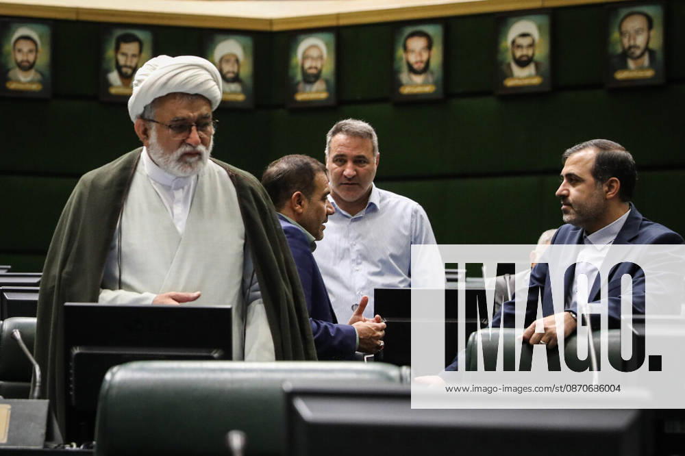A gray-bearded cleric in a white turban stands beside two suited men talking among the parliamentary benches at the Islamic Consultative Assembly in Tehran, Iran, on October 25, 2026. Parliamentary reports said more than two-thirds of lawmakers joined the October 25 open sitting of the Islamic Consultative Assembly, attending either in person or remotely. Tehran Iran - ZUMAi98_ 20261025_zih_i98_063