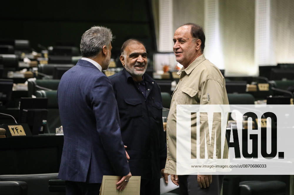 Three suited lawmakers stand in conversation, including a man in a beige jacket, amid the green parliamentary seats at the Islamic Consultative Assembly in Tehran, Iran, on October 25, 2026. The Islamic Consultative Assembly resumed an open sitting in its Tehran chamber with a mix of in-person and remote participation, according to parliamentary reporting. Tehran Iran - ZUMAi98_ 20261025_zih_i98_072