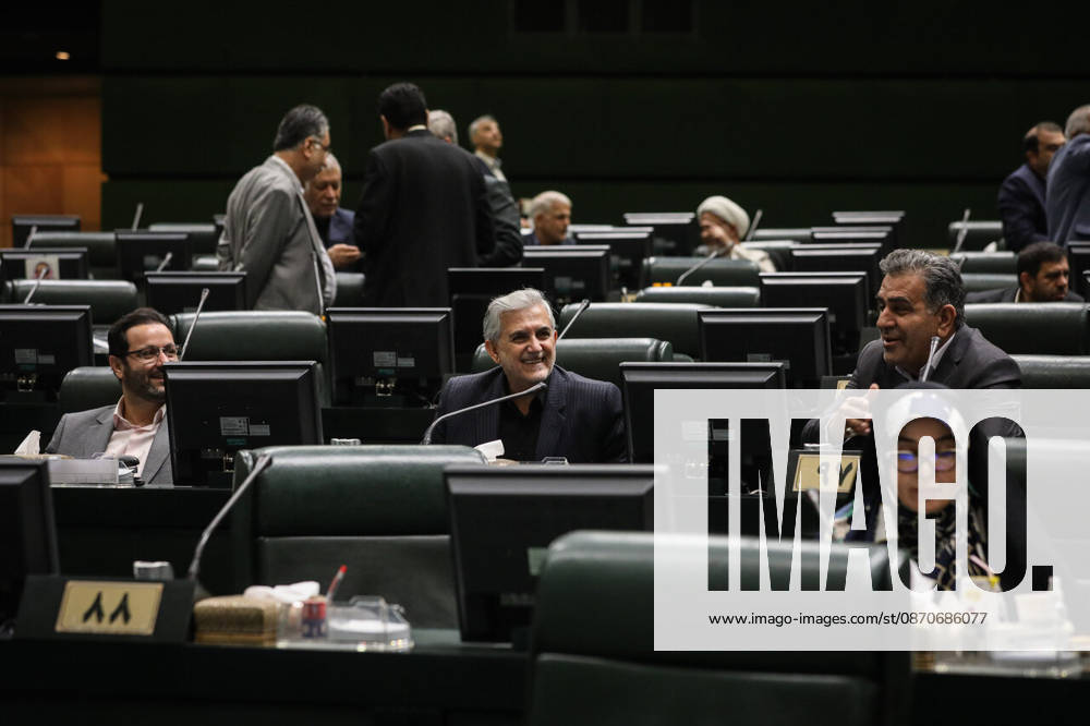 Lawmakers sit at their desks with monitors and microphones as several men stand in conversation farther back at the Islamic Consultative Assembly in Tehran, Iran, on October 25, 2026. The Islamic Consultative Assembly resumed an open sitting in its Tehran chamber with a mix of in-person and remote participation, according to parliamentary reporting. Tehran Iran - ZUMAi98_ 20261025_zih_i98_074
