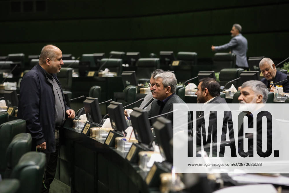 Several male lawmakers gather around their desks while one stands speaking to colleagues seated beside him at the Islamic Consultative Assembly in Tehran, Iran, on October 25, 2026. The Iranian parliament held a hybrid open sitting, with some lawmakers attending in the Tehran chamber and others participating remotely, according to parliamentary reports. Tehran Iran - ZUMAi98_ 20261025_zih_i98_081