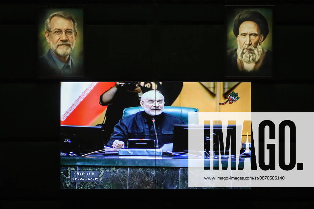 A wall-mounted screen displays a close-up of Mohammad Bagher Ghalibaf seated at the speaker s desk beneath framed portraits at the Islamic Consultative Assembly in Tehran, Iran, on October 25, 2026. Parliamentary reports said more than two-thirds of lawmakers joined the October 25 open sitting of the Islamic Consultative Assembly, attending either in person or remotely. Tehran Iran - ZUMAi98_ 20261025_zih_i98_092