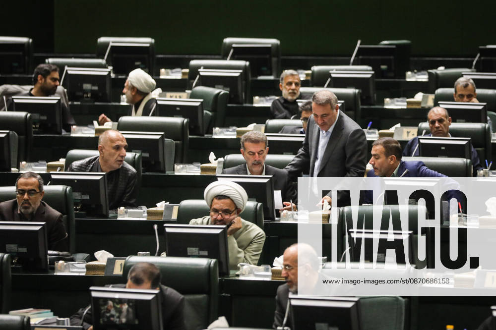 A gray-haired lawmaker leans over a desk to speak with a seated colleague among computer monitors at the Islamic Consultative Assembly in Tehran, Iran, on October 25, 2026. The Iranian parliament held a hybrid open sitting, with some lawmakers attending in the Tehran chamber and others participating remotely, according to parliamentary reports. Tehran Iran - ZUMAi98_ 20261025_zih_i98_099