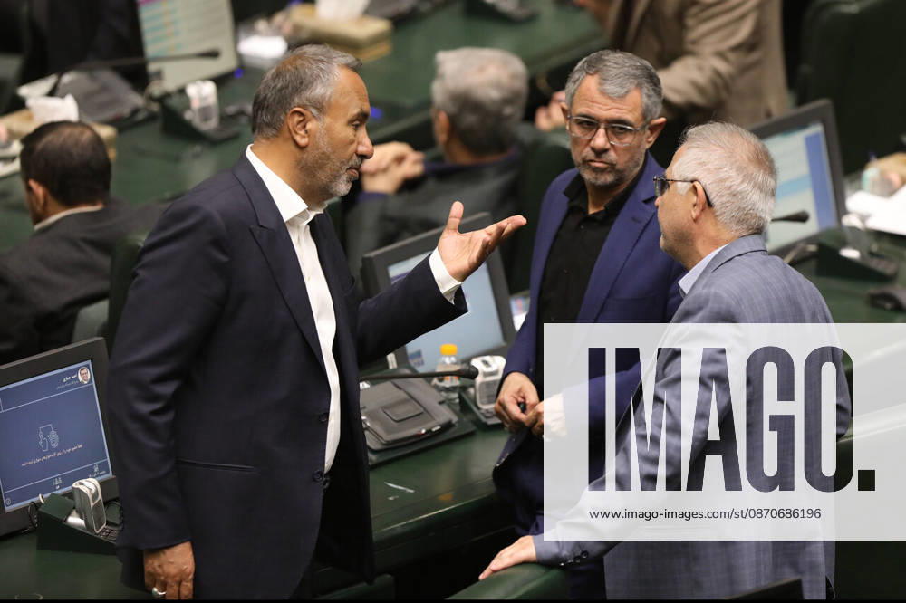 A suited lawmaker gestures with one hand while speaking to two colleagues beside the parliamentary benches at the Islamic Consultative Assembly in Tehran, Iran, on October 25, 2026. The Iranian parliament held a hybrid open sitting, with some lawmakers attending in the Tehran chamber and others participating remotely, according to parliamentary reports. Tehran Iran - ZUMAi98_ 20261025_zih_i98_115