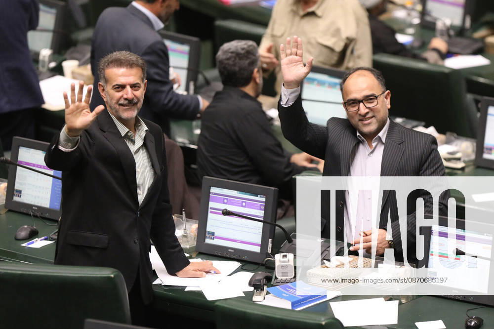 A dark-haired lawmaker raises both hands in greeting while another suited man smiles beside him in the chamber at the Islamic Consultative Assembly in Tehran, Iran, on October 25, 2026. Speaker Mohammad Bagher Ghalibaf chaired the October 25 session, which combined physical attendance at the Islamic Consultative Assembly with participation by video link. Tehran Iran - ZUMAi98_ 20261025_zih_i98_116