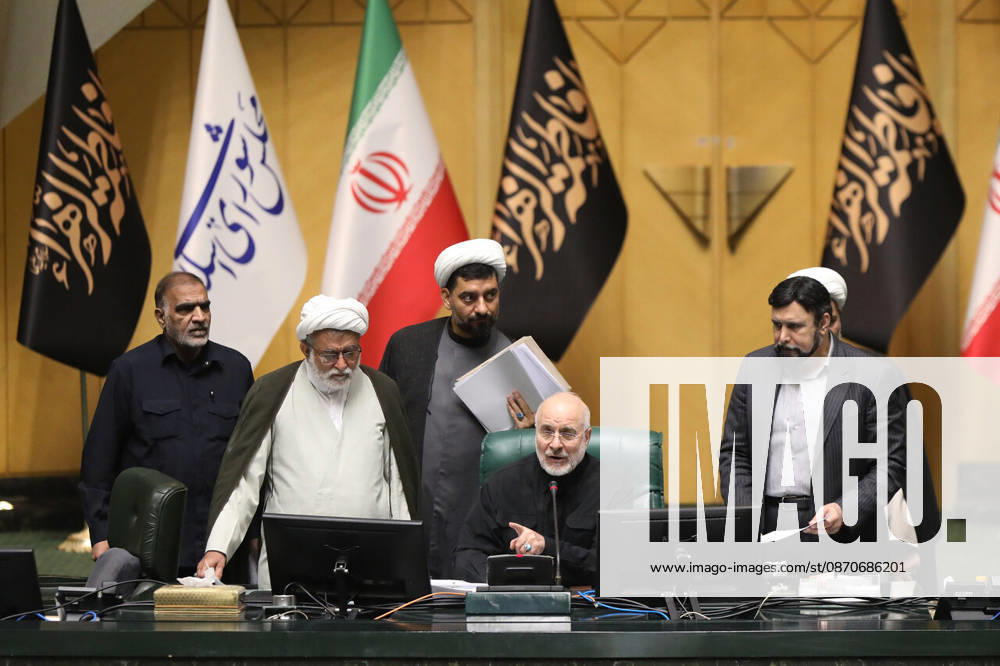 Mohammad Bagher Ghalibaf sits at the presiding desk with four male officials standing beside him beneath Iranian flags at the Islamic Consultative Assembly in Tehran, Iran, on October 25, 2026. Speaker Mohammad Bagher Ghalibaf chaired the October 25 session, which combined physical attendance at the Islamic Consultative Assembly with participation by video link. Tehran Iran - ZUMAi98_ 20261025_zih_i98_119