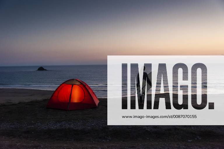 Young woman camping on the beach, carrying surfboard at night model released Symbolfoto UUF15166