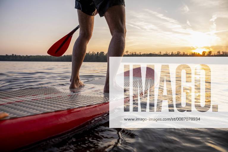 Legs of man standing on paddleboard at sunset model released Symbolfoto FMKF05242