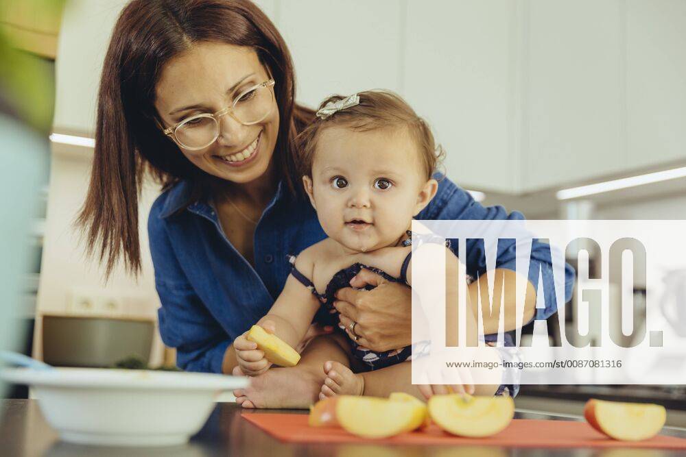 Mother and baby daughter eating apple chunks in kitchen model released Symbolfoto property released MFF04646