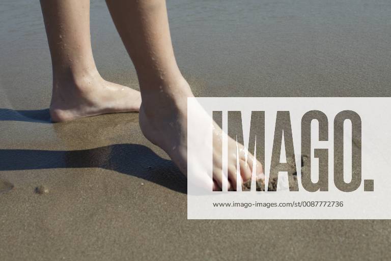 Child drawing in wet sand with foot, cropped