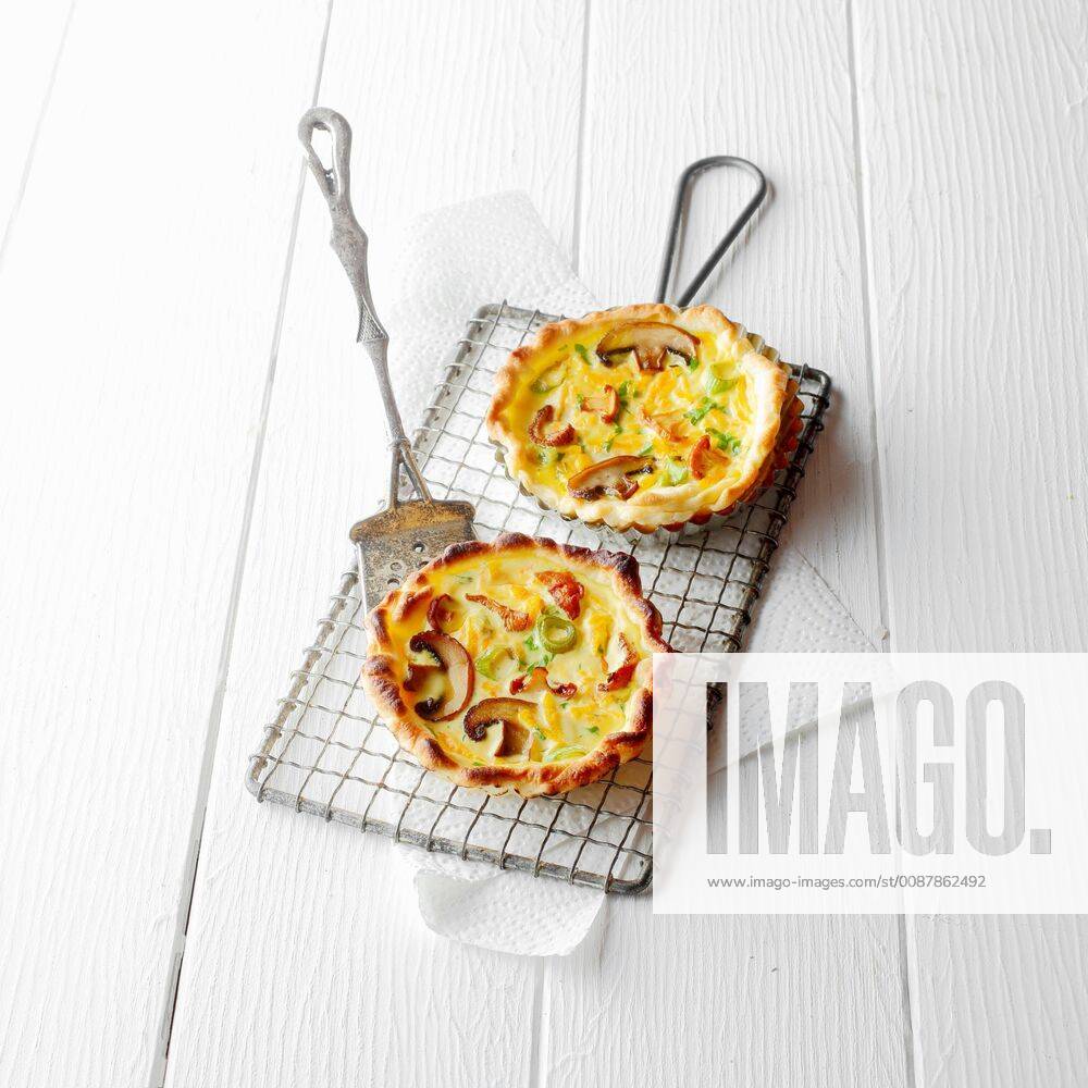 High Angle View of Two Individual Quiche Pies with Mushrooms on Wire Baking Cooling Rack with Metal Lifter on White Wooden Background