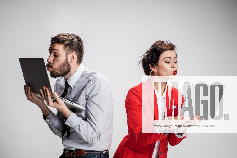 The young businessman and businesswoman with laptops kissing screens on gray background model released Symbolfoto