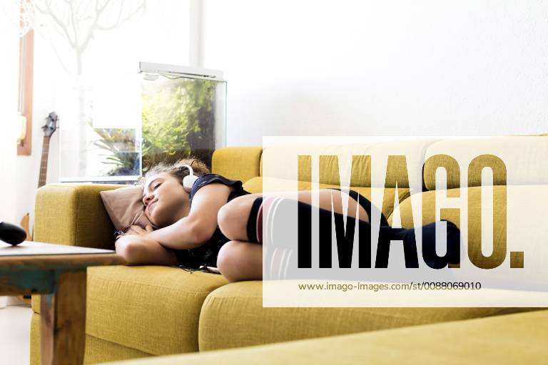 Girl lying on the couch at home listening music with headphones and smartphone model released Symbolfoto property released ERRF00056