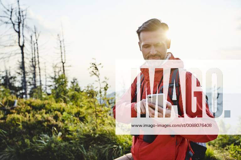 Smiling man checking his cell phone during hiking trip model released Symbolfoto BSZF00740