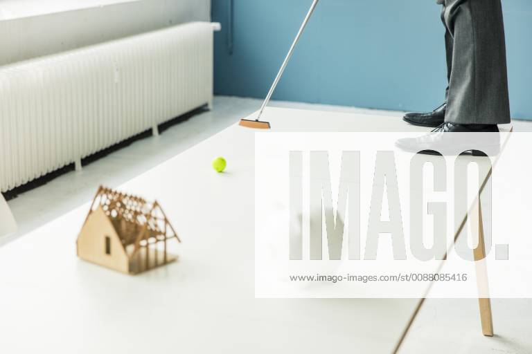 Close-up of businessman playing golf with piggy bank and house model on table in office model released Symbolfoto property released MOEF01396