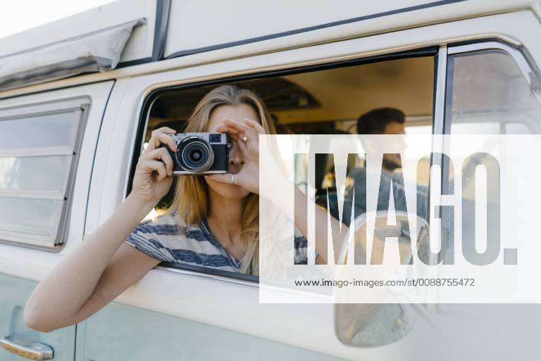 Woman taking picture out of window of a camper van with man driving model released Symbolfoto GUSF01422