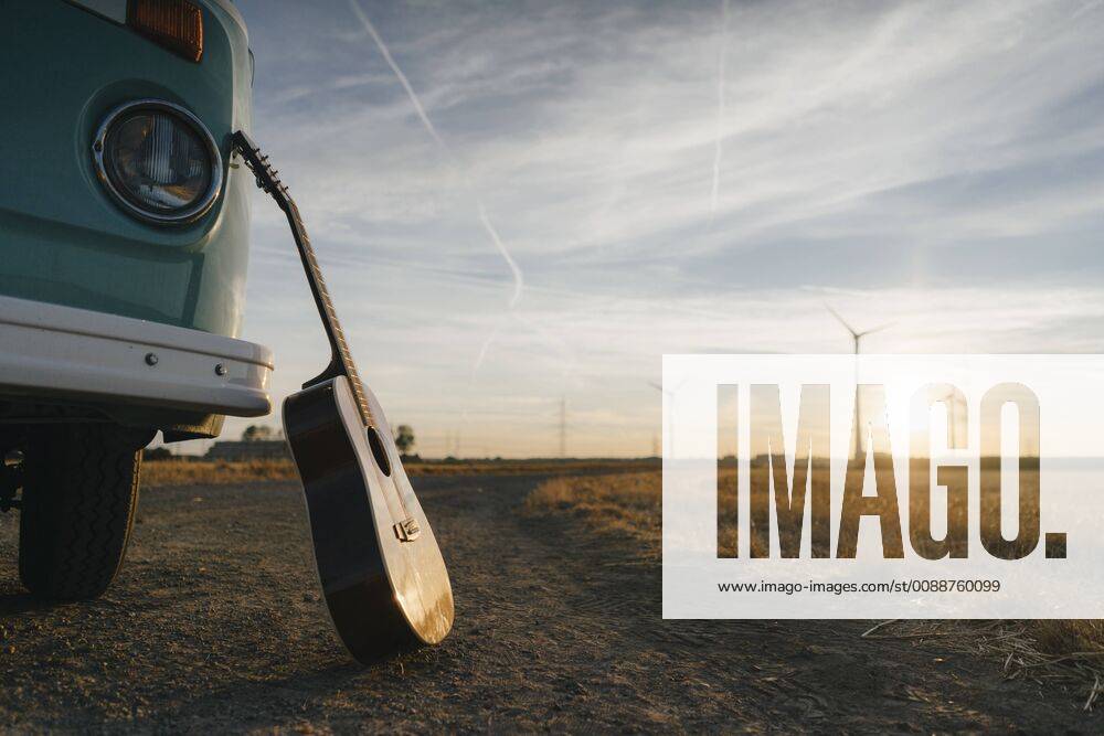 Guitar leaning against camper van in rural landscape with wind turbines at sunset GUSF01404
