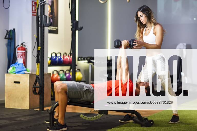 Personal trainer assisting client with weight training, lifting dumbells, lying on bench model released Symbolfoto property released JSMF00492